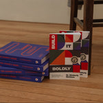 Build It Boldly books displayed beside stacked copies of The Leader’s Work by Dr. Kimberly McGlonn.