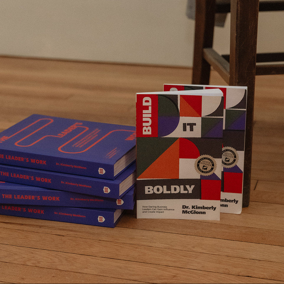 Build It Boldly books displayed beside stacked copies of The Leader’s Work by Dr. Kimberly McGlonn.