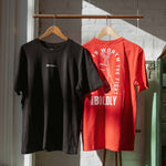Black and red Build It Boldly t-shirts hanging on wooden hangers in sunlight, showing the front logo on the black shirt and “The Future Is Worth the Fight” boxing gloves graphic on the red shirt.