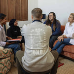 Person seated in a group setting wearing a heather gray Build It Boldly sweatshirt with “The Future Is Worth the Fight” boxing gloves graphic on the back.