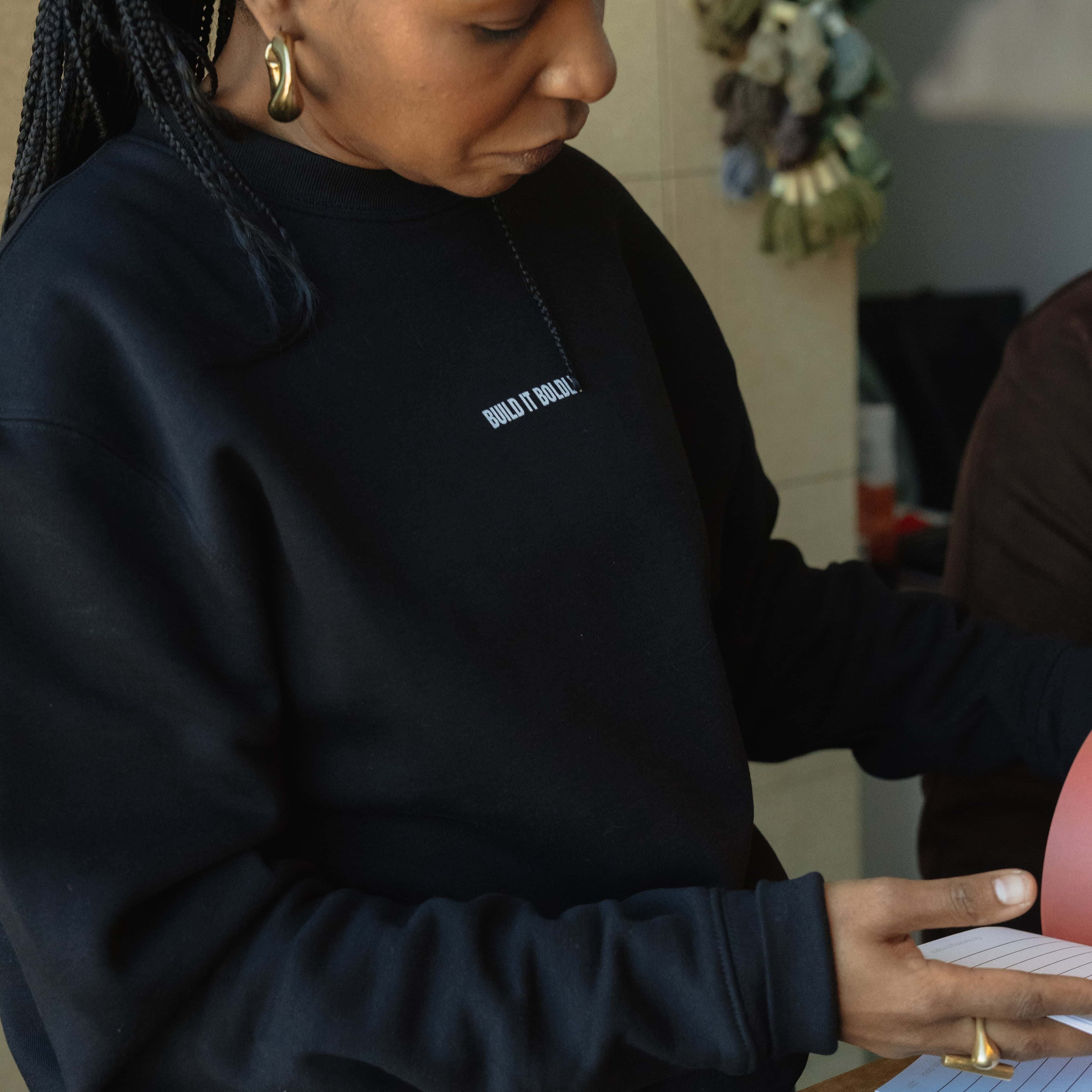 Close-up of Dr. Kimberly McGlonn wearing a black Build It Boldly sweatshirt while holding an open journal
