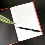 Open Inner Audit Journal with lined pages, a black pen, and a green plant leaf on a dark desk, styled for reflective writing and leadership journaling.