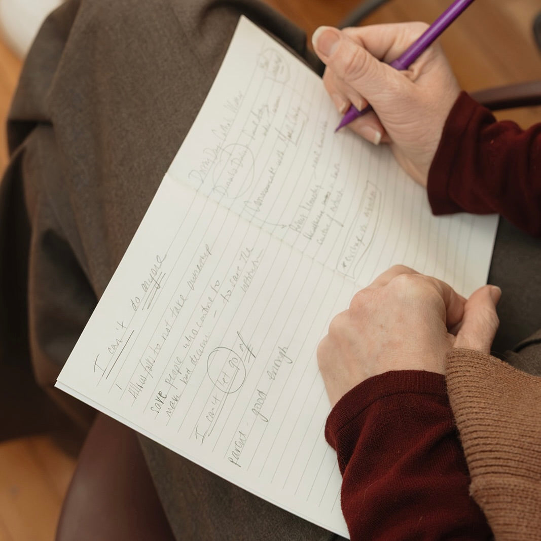 Person writing reflective leadership notes in a notebook during a group coaching or workshop session