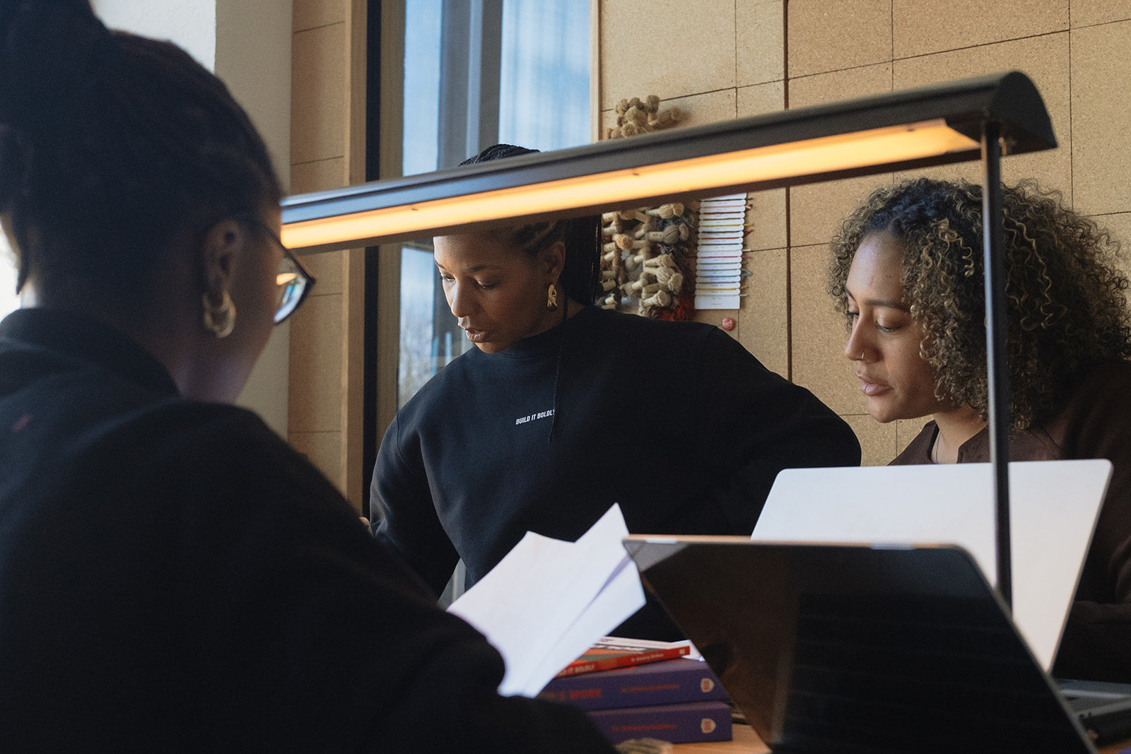 Small group of professionals collaborating at a table with laptops and books, engaged in focused leadership development and intentional work