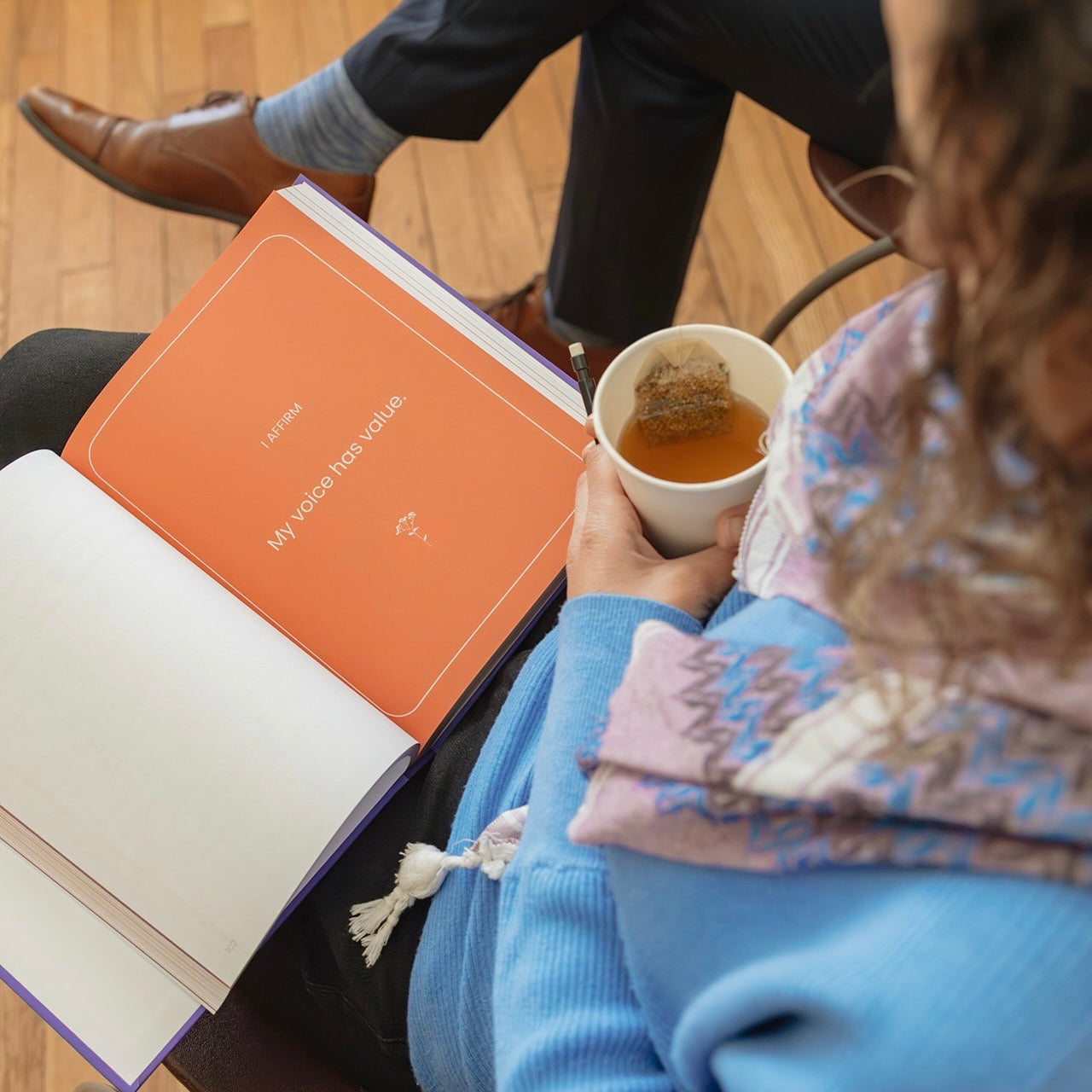 Person reading a leadership workbook with affirmation “My voice has value” while holding tea in a reflective setting