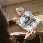 Person reading Build It Boldly by Dr. Kimberly McGlonn at a table with coffee in natural light.