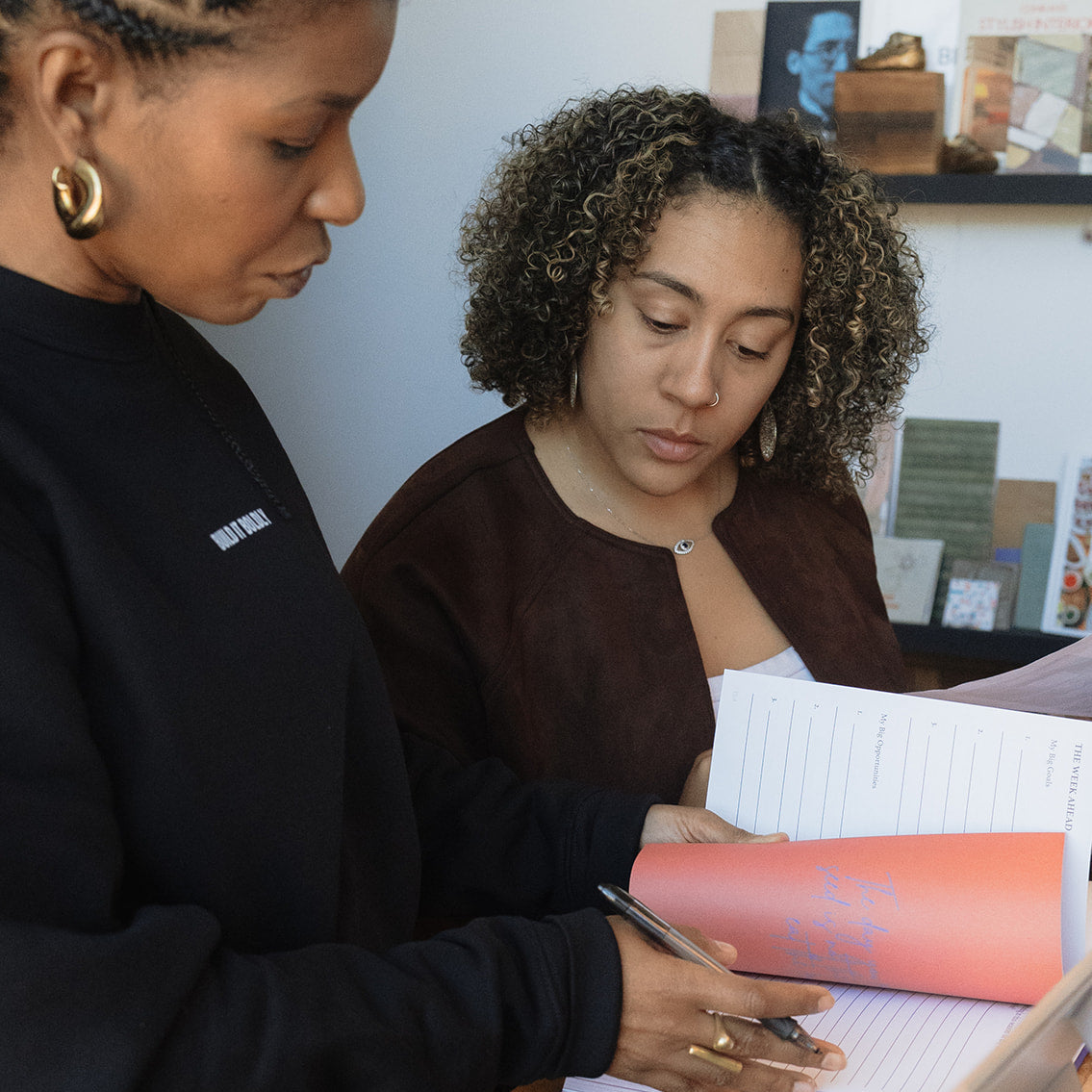 Dr. Kimberly McGlonn and another professional reviewing The Leader’s Work leadership workbook during a collaborative discussion.